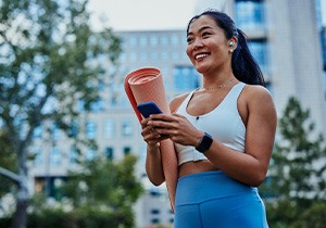 Smiling woman with yoga mat walking in park