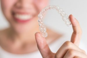 Woman holding an Invisalign tray with her face blurred into the background