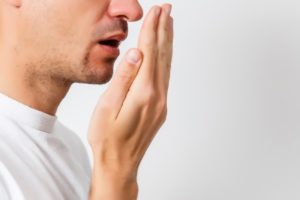 Man smelling bad breath while wearing a white t shirt