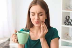 Woman drinking cup of coffee in pain with hand on cheek