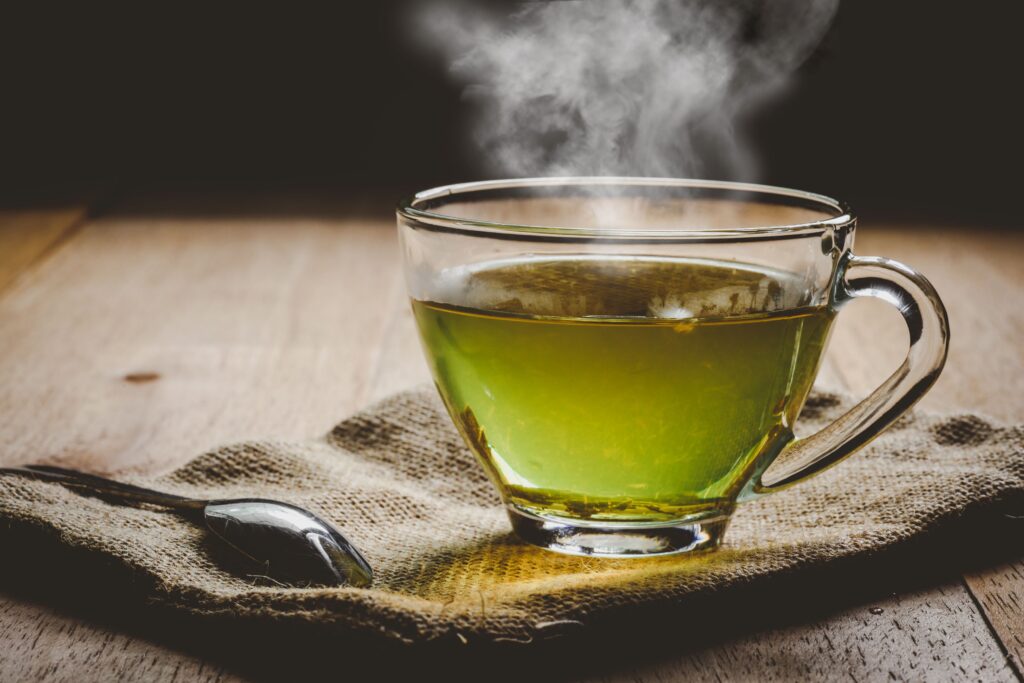 Cup of green tea sitting on napkin next to spoon on wooden surface